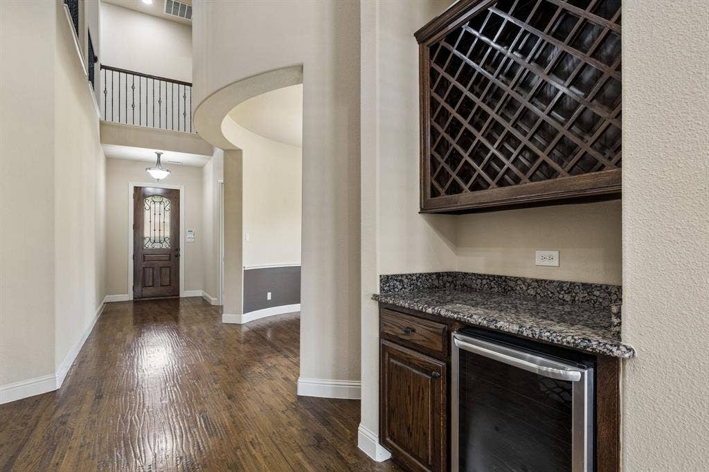 6448 Fire Creek Trail, Frisco, TX 75036 Built-in cabinetry featuring a stone-top counter, wine storage, and under-counter cooling unit, highlighted by wood-finish flooring, high ceilings, and metal stair railing