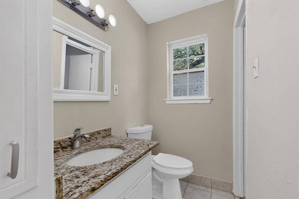 9651 Cherry Street, Frisco, TX 75033 Stone-topped vanity with an integrated oval sink, three-light wall-mounted fixture, framed vanity mirror, and ceramic tile flooring