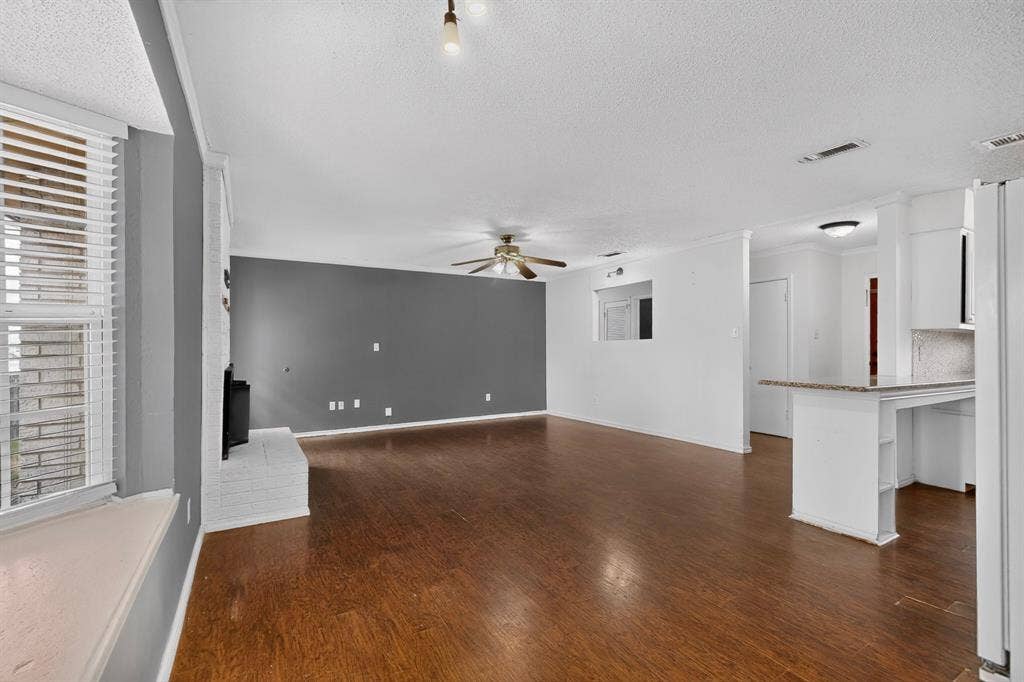 9651 Cherry Street, Frisco, TX 75033 Open-concept interior featuring wood-finish flooring, a white painted brick fireplace, a built-in kitchen breakfast bar with stone-surface countertop, and a window seat