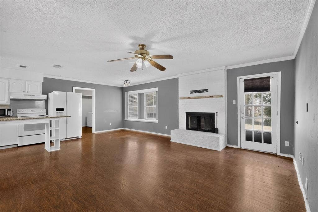 9651 Cherry Street, Frisco, TX 75033 Wood-finish flooring, white painted brick fireplace with a mantle, built-in kitchen cabinetry, ceiling fan, and multi-light glass panel exterior door