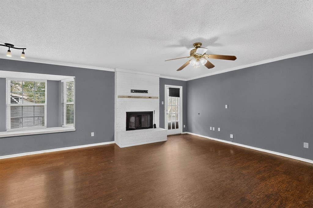 9651 Cherry Street, Frisco, TX 75033 Living area featuring wood-finish flooring, a painted brick fireplace with a wood mantel, a multi-paneled bay window, and a ceiling fan with integrated lighting