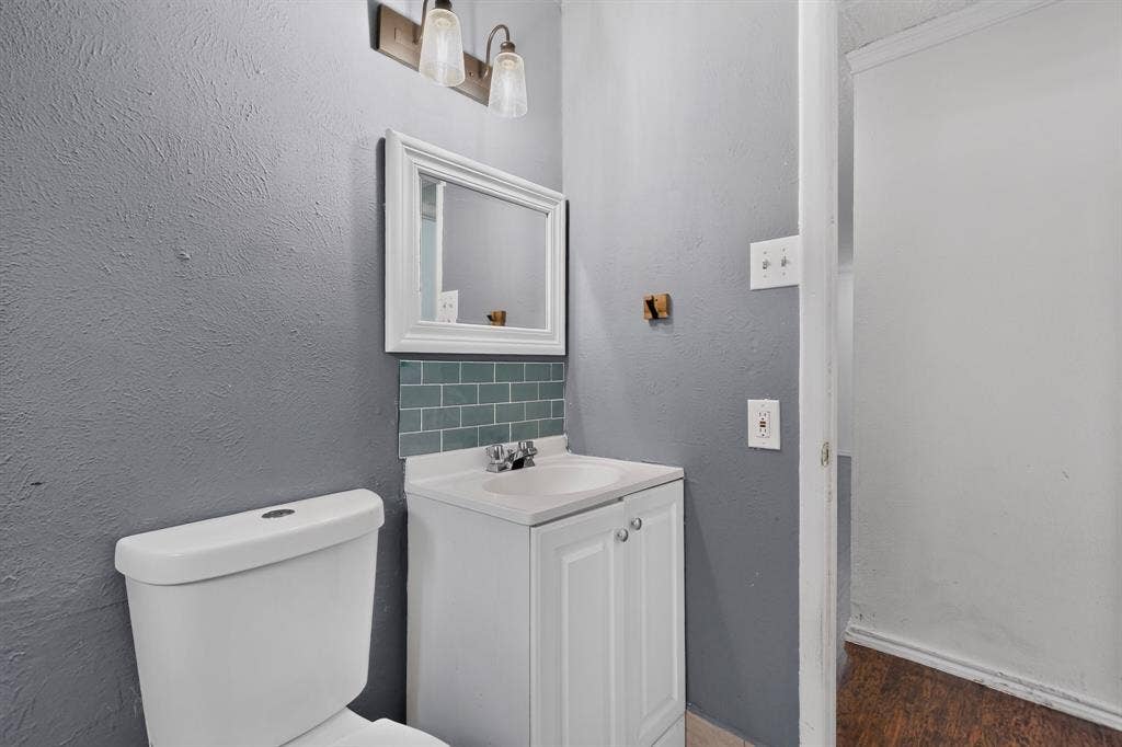 9651 Cherry Street, Frisco, TX 75033 White vanity with integrated sink, teal subway tile backsplash, wall-mounted light fixture, framed mirror, and porcelain toilet