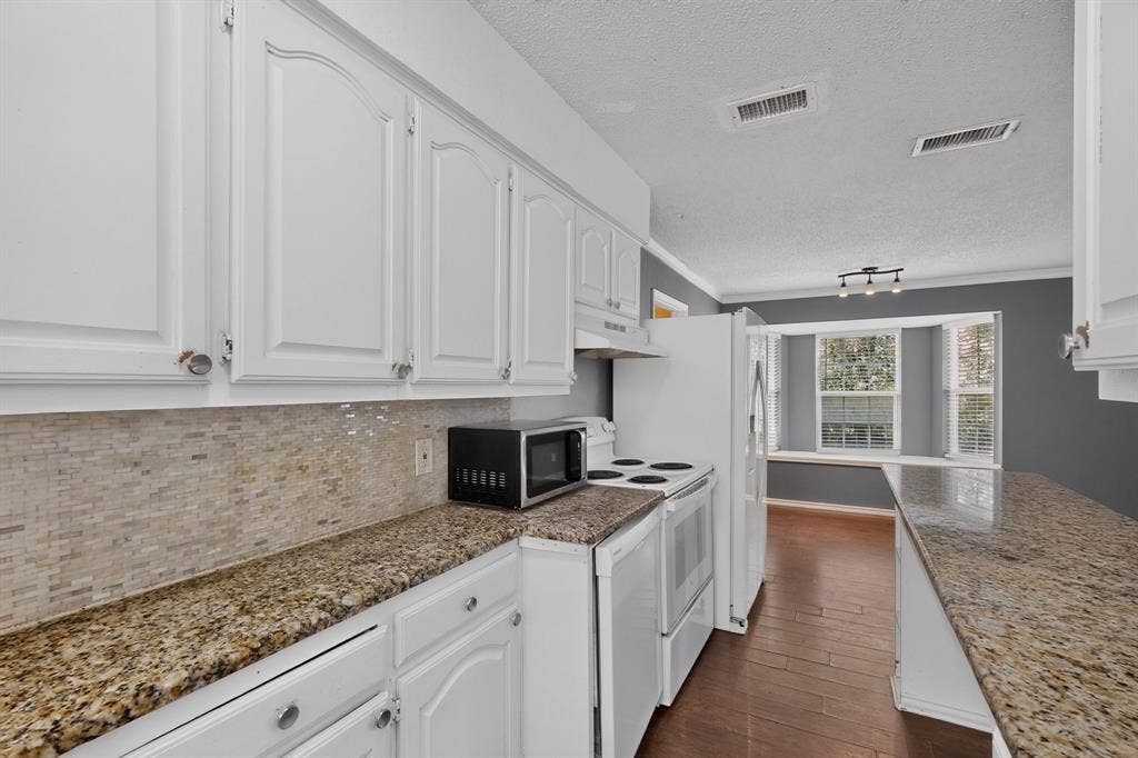 9651 Cherry Street, Frisco, TX 75033 Kitchen featuring white cabinetry, stone-finish countertops, textured stone backsplash, wood-finish flooring, and a bay window