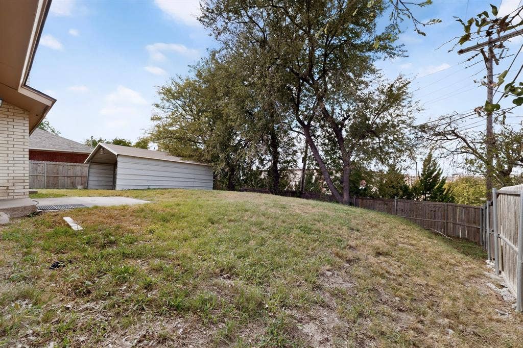 9651 Cherry Street, Frisco, TX 75033 Backyard featuring a grass lawn, mature trees, metal storage structure, and wood privacy fencing