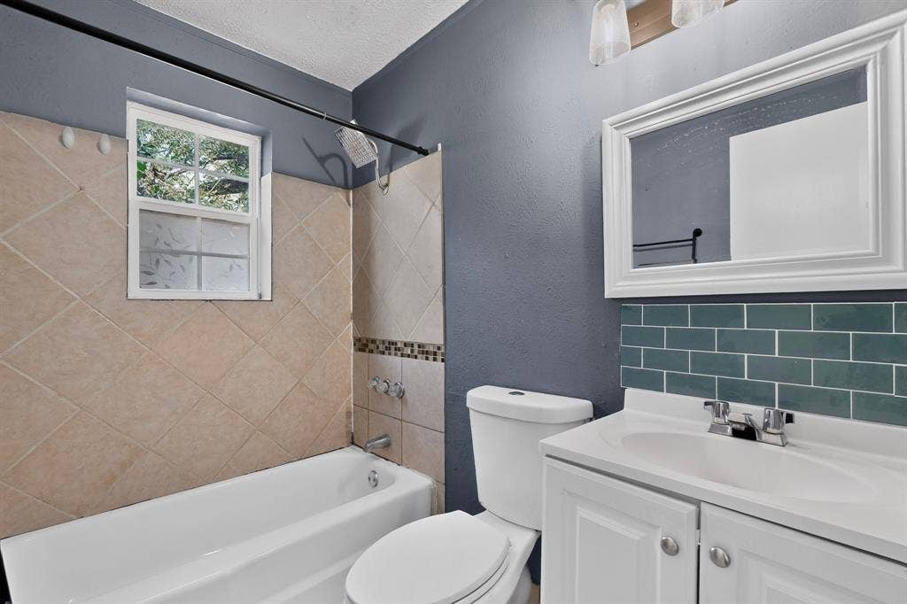9651 Cherry Street, Frisco, TX 75033 Bathroom featuring a white vanity with an integrated sink, teal subway tile backsplash, white framed wall mirror, and tub-shower combination with diagonal wall tiling