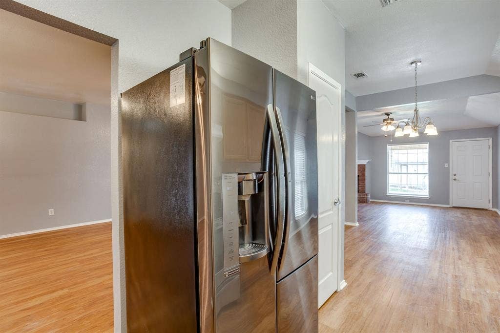 6221 St Leonard Drive, Arlington, TX 76001 Stainless steel French door refrigerator, wood-finish flooring, multi-light hanging chandelier, and brick-faced fireplace
