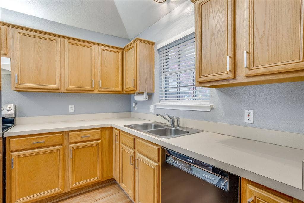 6221 St Leonard Drive, Arlington, TX 76001 Kitchen featuring wood cabinetry, solid-surface countertops, dual-basin stainless steel sink, and integrated dishwasher