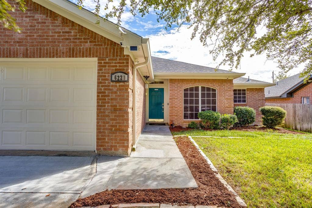 6221 St Leonard Drive, Arlington, TX 76001 Brick exterior featuring an attached two-car garage, arched window, concrete walkway, and manicured landscaping