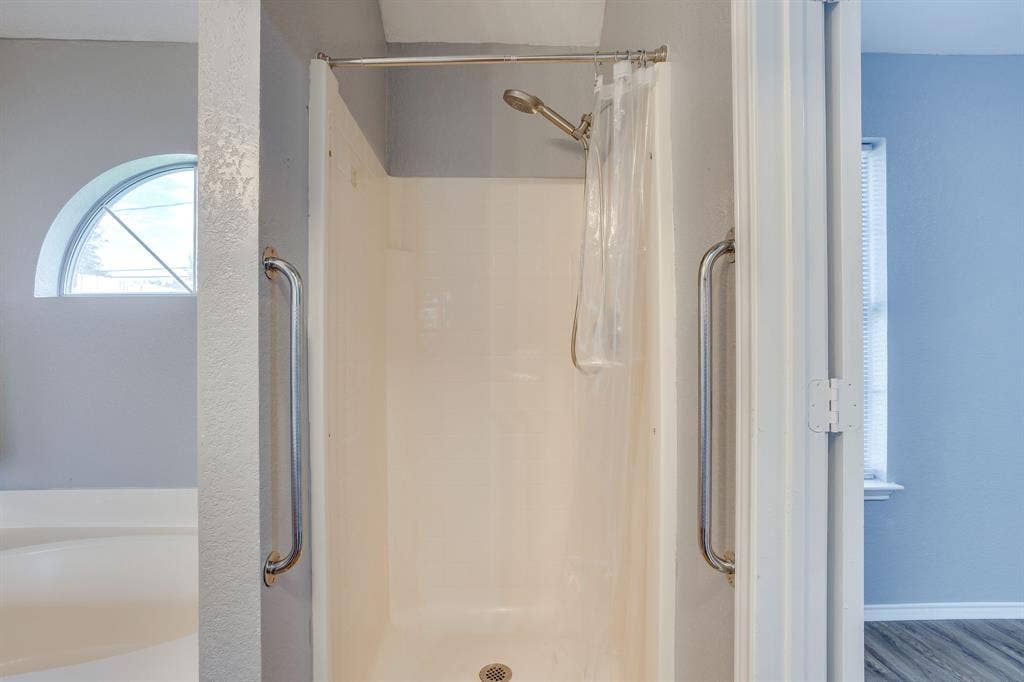6221 St Leonard Drive, Arlington, TX 76001 Shower enclosure featuring metal grab bars, adjustable wall-mounted shower head, and arched window