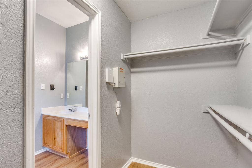 6221 St Leonard Drive, Arlington, TX 76001 Walk-in closet featuring tiered shelving and wood-finish flooring, complemented by a bathroom area with built-in wood cabinetry, a white countertop, and wall-mounted vanity mirror