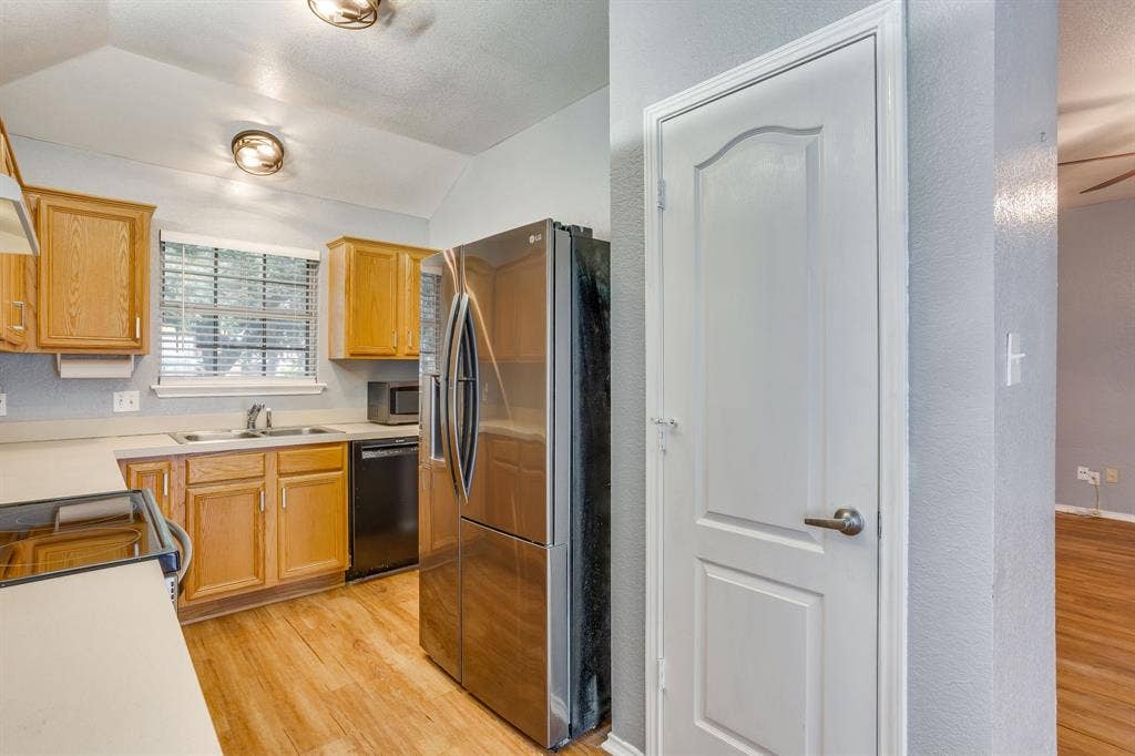 6221 St Leonard Drive, Arlington, TX 76001 Kitchen featuring shaker-style cabinetry, stainless steel refrigerator, solid-surface countertops, dual-basin stainless steel sink, and wood-finish flooring