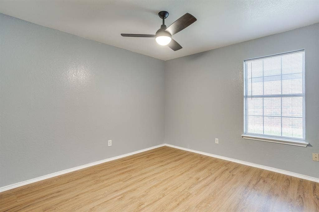 6221 St Leonard Drive, Arlington, TX 76001 Interior room featuring light-toned walls, wood-finish flooring, a single window with horizontal blinds, and a dark-finish ceiling fan with integrated lighting