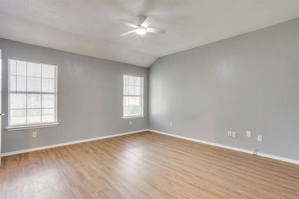 6221 St Leonard Drive, Arlington, TX 76001 Room featuring wood-finish flooring, vaulted ceilings, neutral wall paint, two grid-pattern windows, and a central ceiling fan with integrated lighting