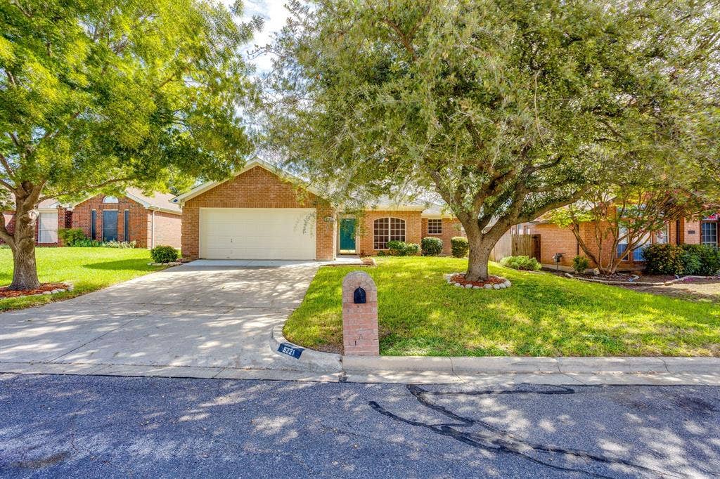 6221 St Leonard Drive, Arlington, TX 76001 Single-story brick exterior featuring a multi-car garage, arched window accents, mature trees, and a concrete driveway