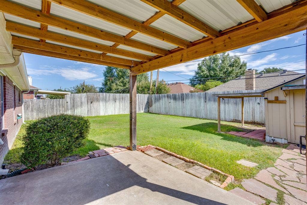 6221 St Leonard Drive, Arlington, TX 76001 Covered patio featuring an exposed wood-beam ceiling, concrete flooring, stone-bordered landscaping, and a fenced backyard