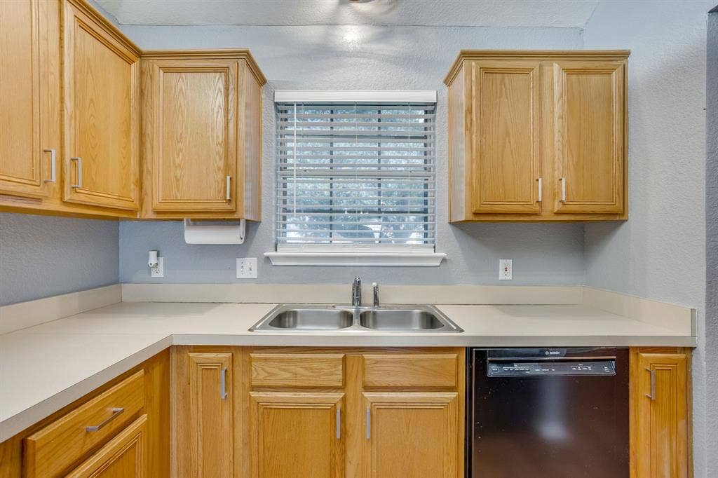 6221 St Leonard Drive, Arlington, TX 76001 Kitchen featuring natural wood-finish cabinetry, solid-surface countertops, dual-basin stainless steel sink, and built-in black dishwasher