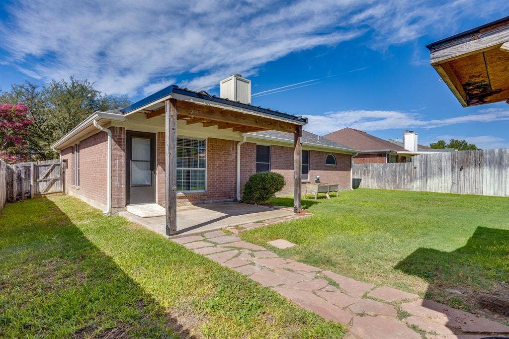 6221 St Leonard Drive, Arlington, TX 76001 Exterior brick facade featuring a covered concrete patio, stone walkway, and perimeter wood fencing