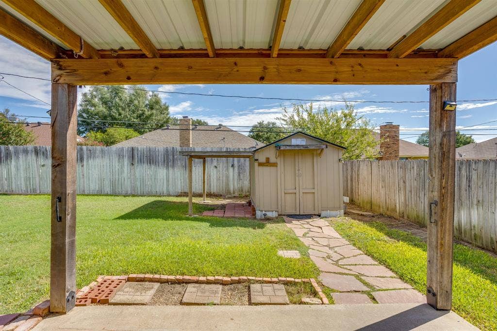 6221 St Leonard Drive, Arlington, TX 76001 Covered patio with exposed timber framing, detached storage shed, stone paver walkway, and wood privacy fencing