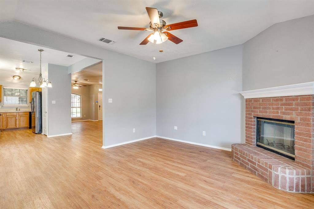 6221 St Leonard Drive, Arlington, TX 76001 Red brick fireplace with a decorative mantel, wood-finish flooring, and ceiling fan with integrated lighting