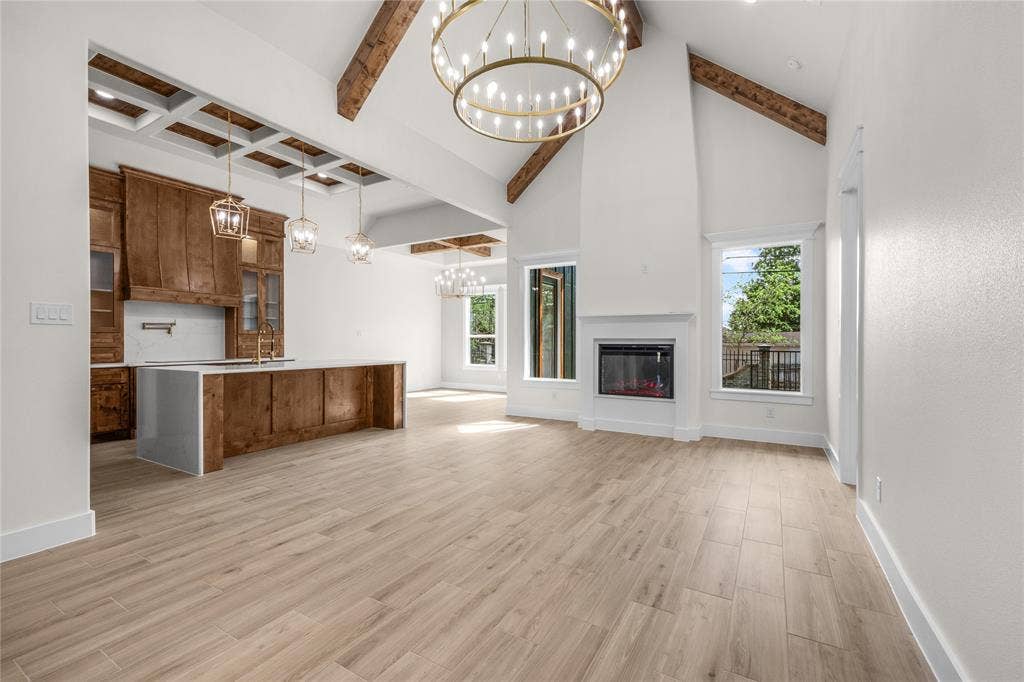 Vaulted ceilings with exposed wooden beams, wood-finish flooring, custom wooden cabinetry, a built-in fireplace, and expansive custom chandeliers