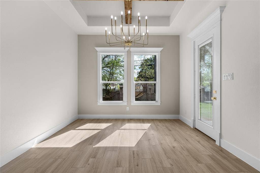 Tray ceiling featuring a stained wood beam, complemented by a multi-arm chandelier, wood-finish flooring, and a glass-paneled exterior door