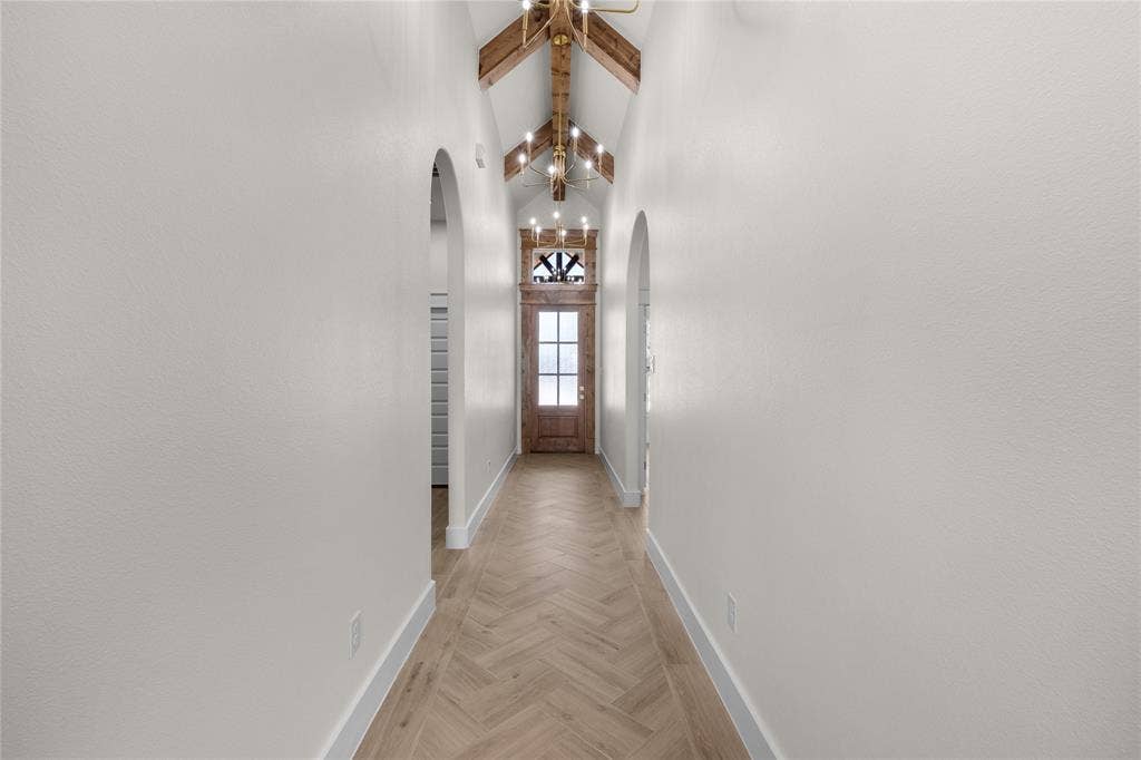 Vaulted ceiling featuring exposed wood beams, herringbone-patterned wood-finish flooring, arched doorways, and a wood-framed entry door with a decorative transom window