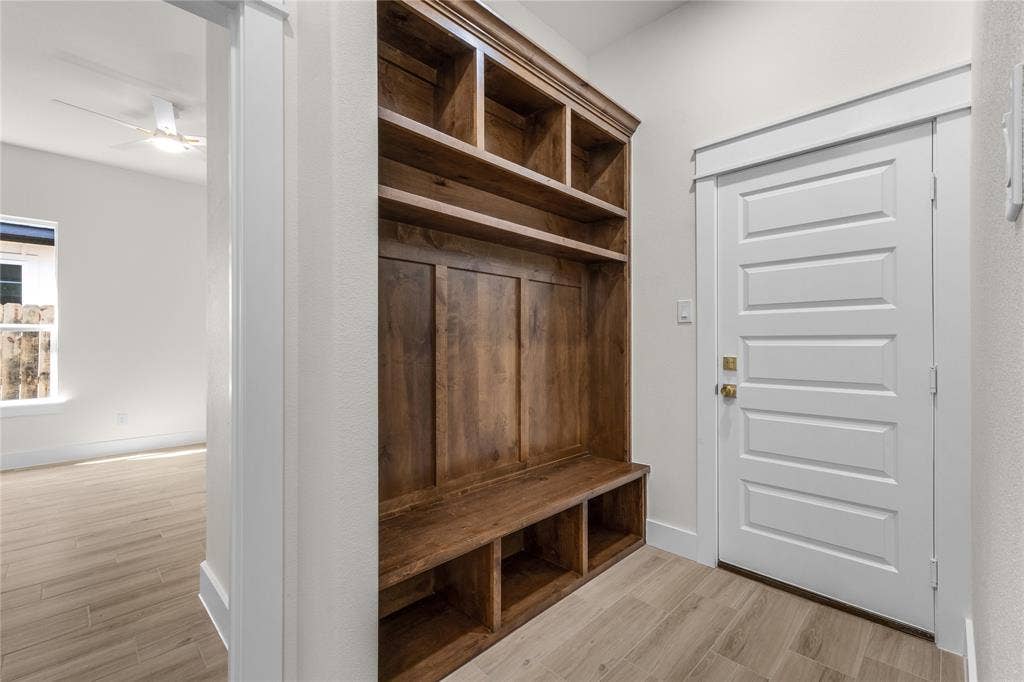 Built-in wooden mudroom cabinetry featuring upper cubbies, paneled backing, and lower open shelving, complemented by wood-finish tile flooring and a five-panel interior door