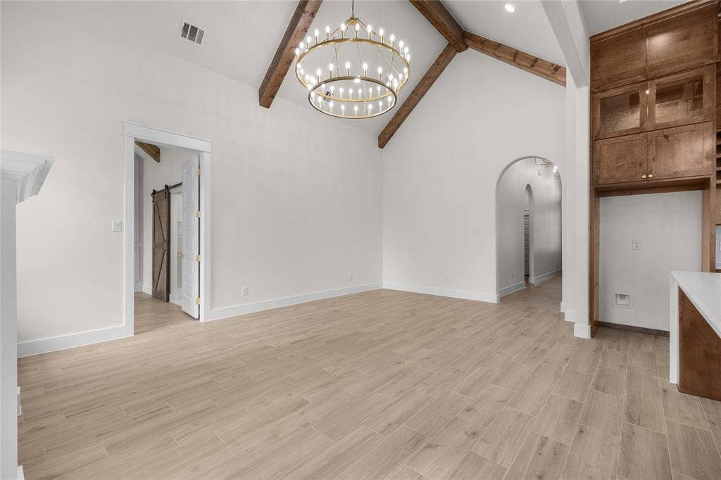 Vaulted ceilings with exposed wood beams, circular tiered chandelier, wood-finish flooring, floor-to-ceiling custom wood cabinetry, and arched doorways