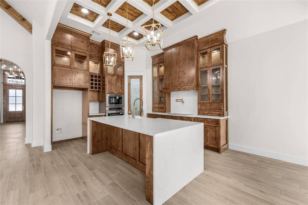 Kitchen featuring custom floor-to-ceiling cabinetry, a center island with a waterfall countertop, coffered ceiling with wood-finish insets, pendant lighting, and wood-finish flooring