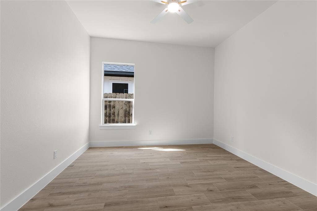 Interior space featuring wood-finish flooring, crisp neutral wall paint, and a white ceiling fan with integrated lighting