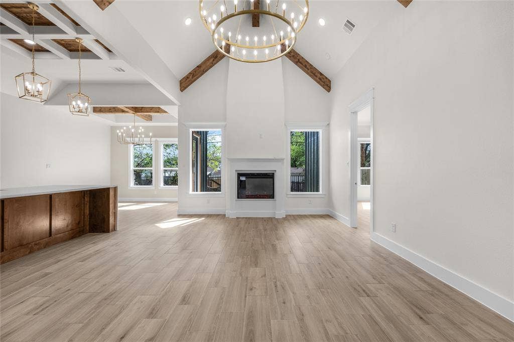 Vaulted ceiling featuring exposed wood beams, a central fireplace, wood-finish flooring, and decorative chandeliers