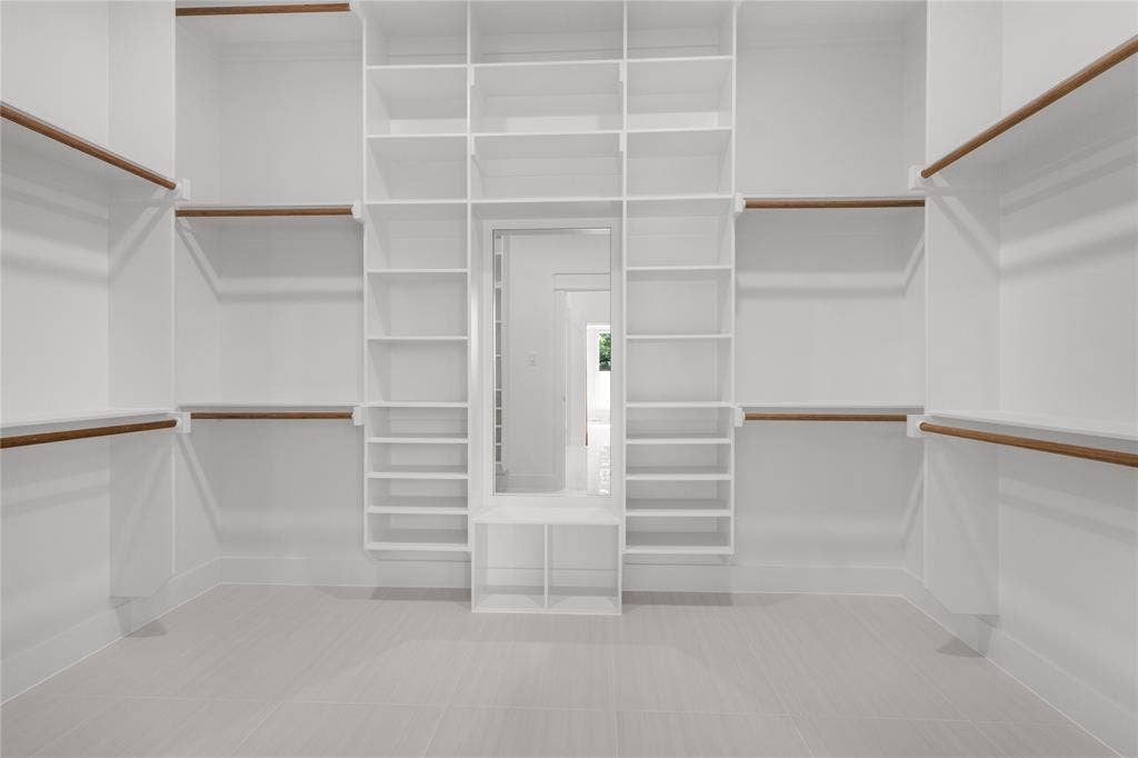 Custom walk-in closet featuring floor-to-ceiling white shelving, integrated hanging rods with wood finishes, a central built-in vanity mirror, and ceramic tile flooring