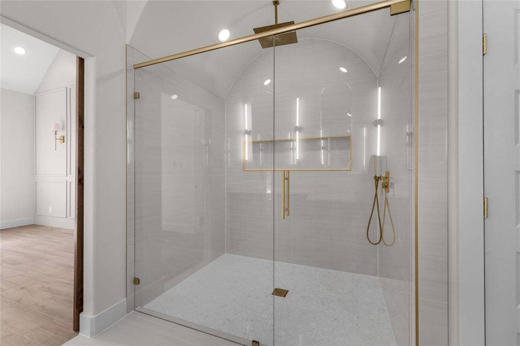Walk-in shower featuring an arched ceiling, floor-to-ceiling tile surround, gold-finish hardware, a rainfall shower head with handheld sprayer, and a built-in recessed niche