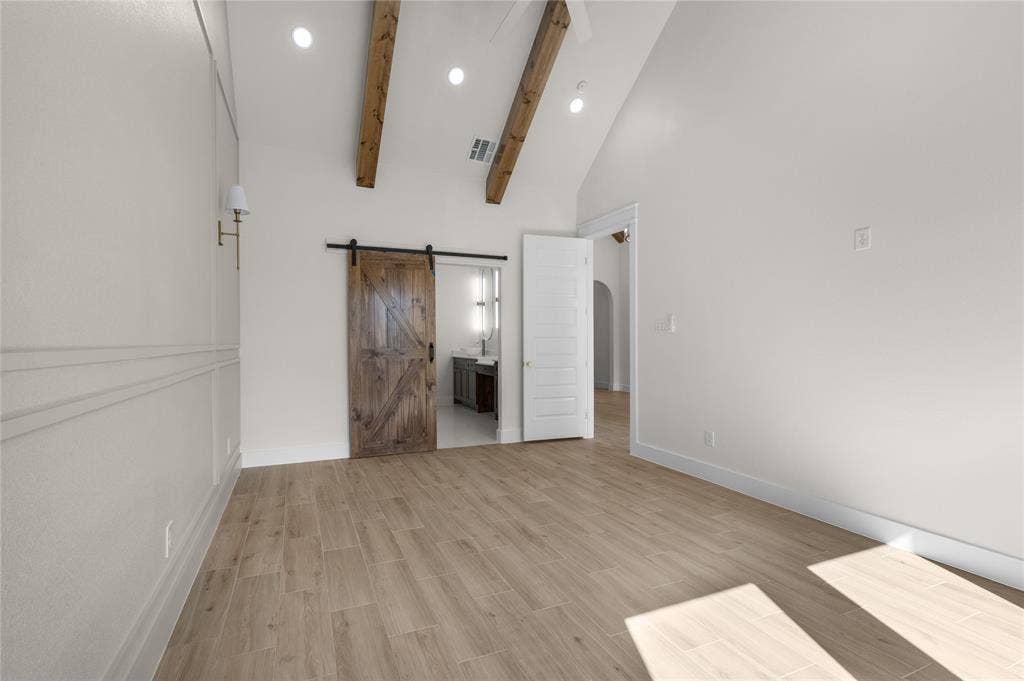 Vaulted ceiling featuring exposed wood beams, wood-finish flooring, sliding barn door, wainscoting wall paneling, and recessed lighting