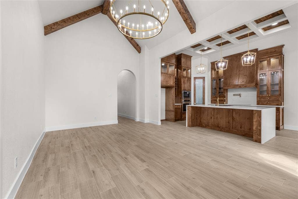 Vaulted ceiling with exposed wood beams, wood-finish tile flooring, custom cabinetry, kitchen island with stone countertop, and coffered ceiling detail