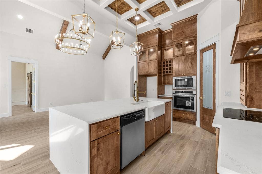 Kitchen featuring wood-finish flooring, coffered ceiling with inset wood paneling, wood cabinetry with integrated wine storage, quartz countertops, and an island with an apron-front sink