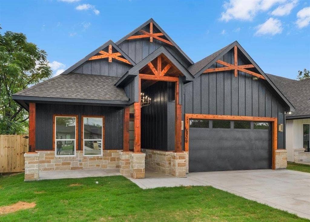 Modern exterior featuring vertical board-and-batten siding, decorative timber trusses, stone veneer masonry, and a covered front porch with timber posts