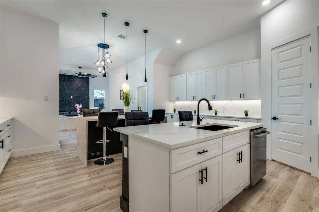 2802 Guymon Street, Dallas, TX 75212 Kitchen featuring a central island with a quartz countertop, white shaker-style cabinetry, matte black hardware, integrated stainless steel dishwasher, and wood-finish flooring