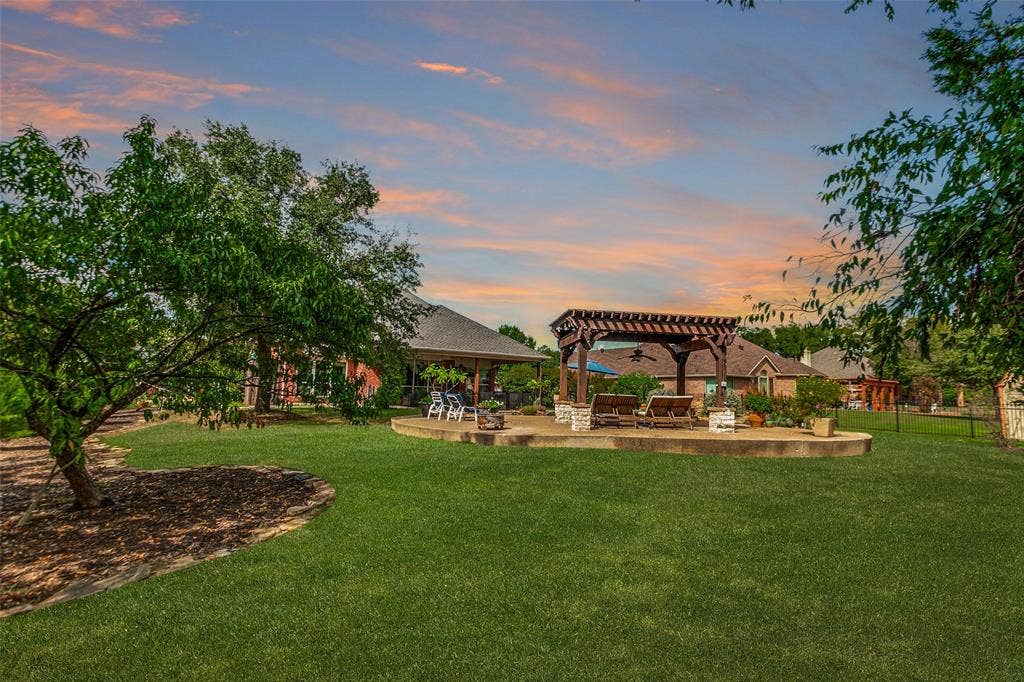 214 Stanford Ct. - Expansive backyard view showcasing the spacious lawn, rear of the pergola, and back of the home. AI generated sunset