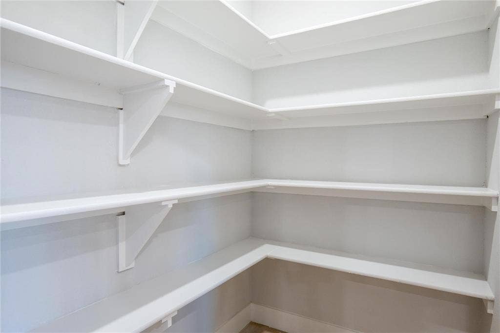 Walk-in storage space featuring multi-level white shelving supported by integrated wall brackets