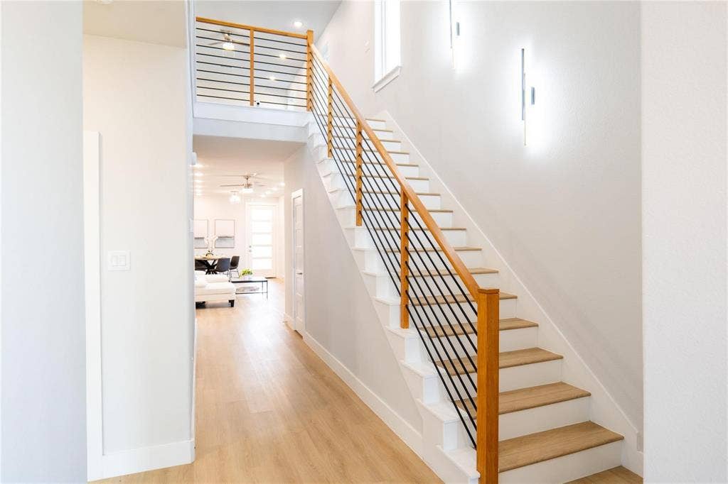 Staircase featuring wood-finish treads, a wood handrail, and horizontal metal balusters, complemented by wall-mounted vertical light fixtures and wood-finish flooring