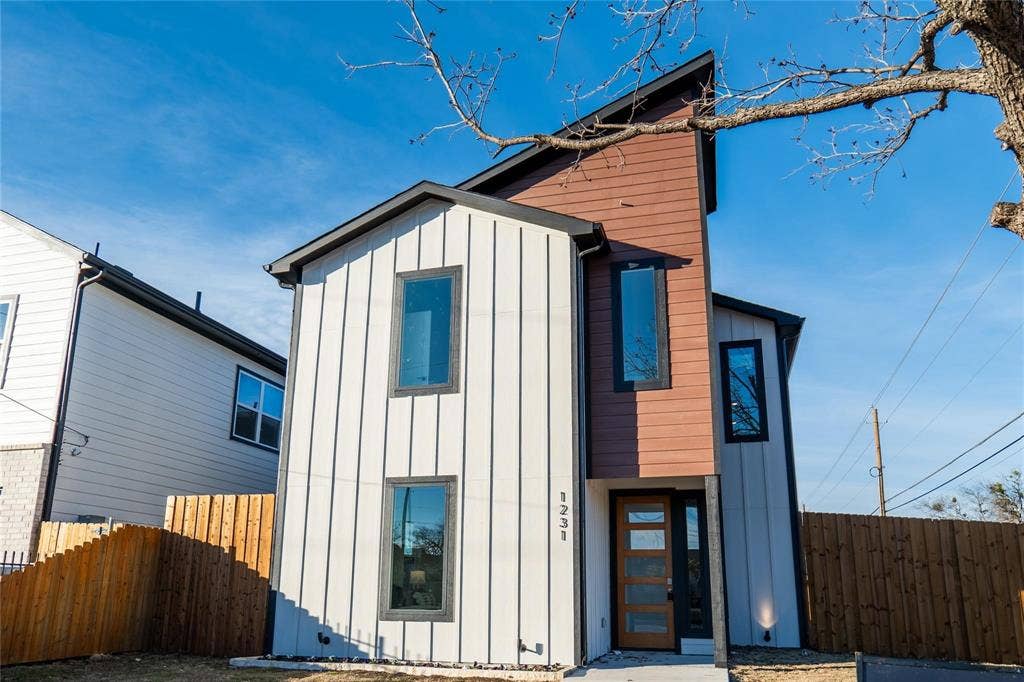 Modern architectural exterior featuring vertical panel siding, horizontal wood-finish accents, a high-pitch roofline, and a multi-pane glass entry door