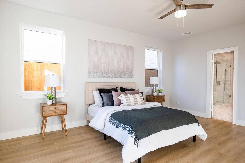 Neutral-toned bedroom featuring wood-finish flooring, dual windows, and an integrated ceiling fan with light fixture