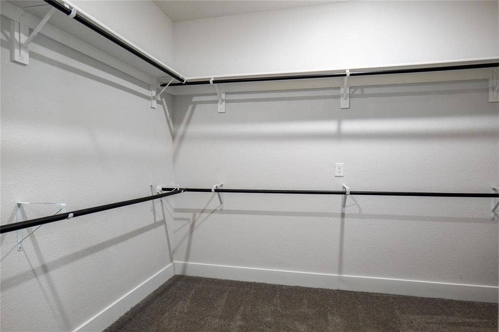 Walk-in closet featuring two-tier storage, wall-mounted white shelving, dark finish metal hanging rods, and carpeted flooring