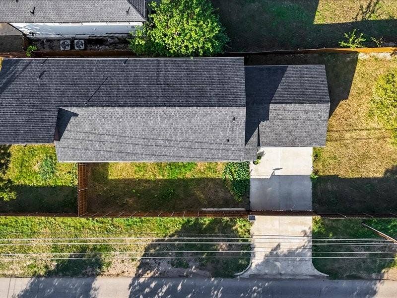 Aerial perspective featuring a shingled roof, concrete driveway, and fenced yard area