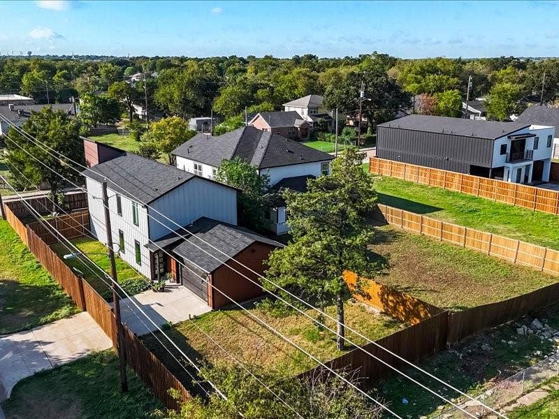 Aerial perspective of multi-level exterior featuring vertical siding, a composition shingle roof, a concrete driveway, and enclosed backyard fencing