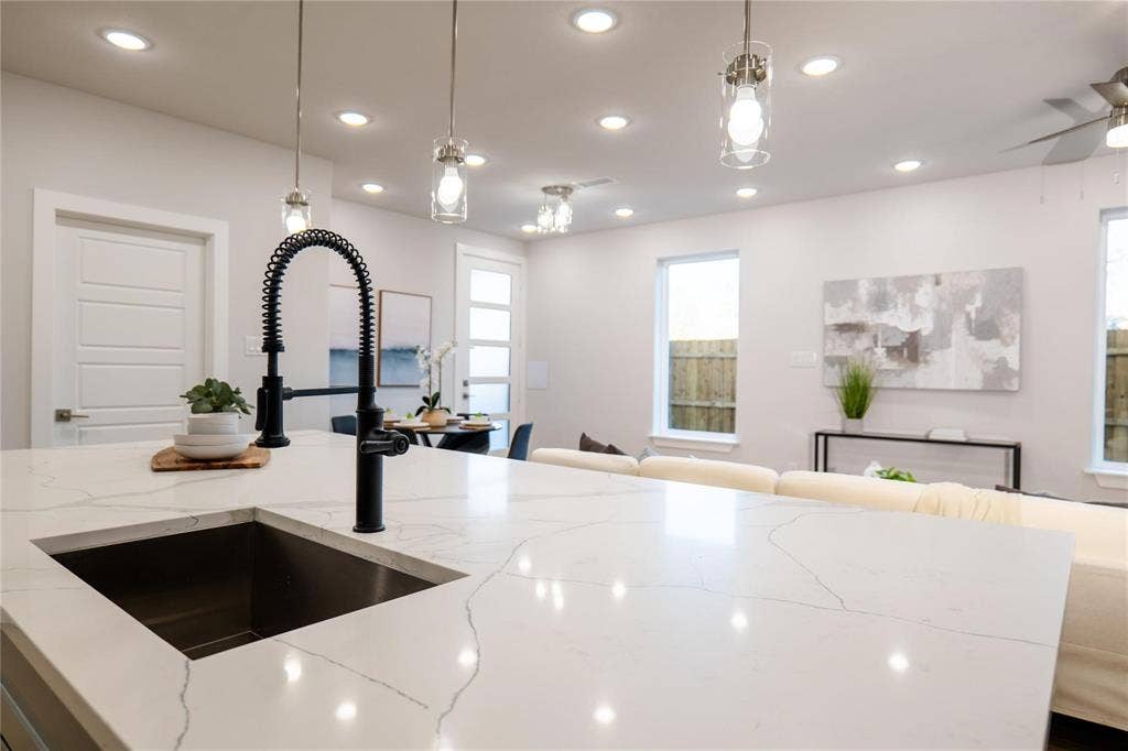 Kitchen featuring a white veined countertop, undermount sink with a matte black spring-neck faucet, glass pendant lighting, and recessed ceiling lights