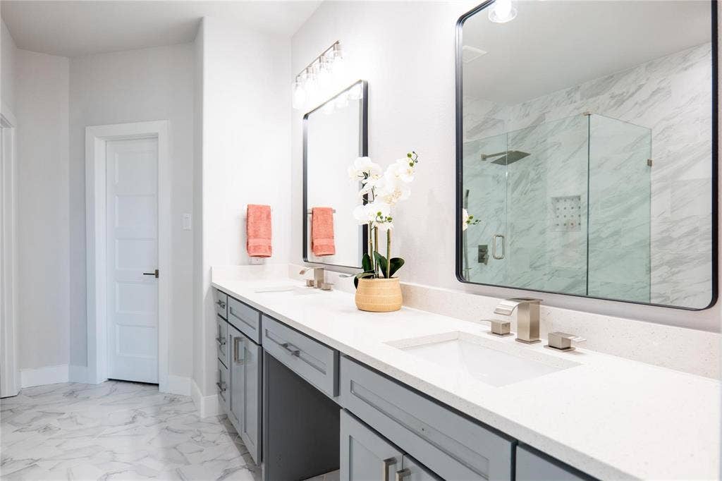 Dual-vanity cabinetry with matte-finish hardware, solid-surface countertops, rectangular undermount sinks, framed wall mirrors, and walk-in shower with glass enclosure