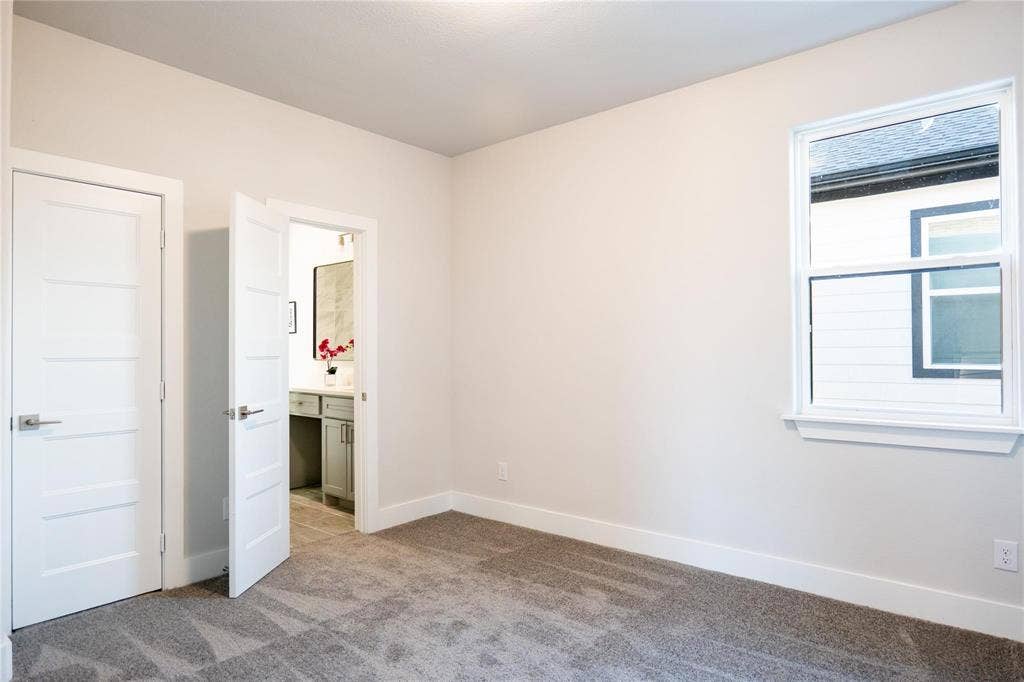 Neutral-toned interior featuring carpeted flooring, a single-hung window with a sill, and two solid-core interior doors with metallic lever handles