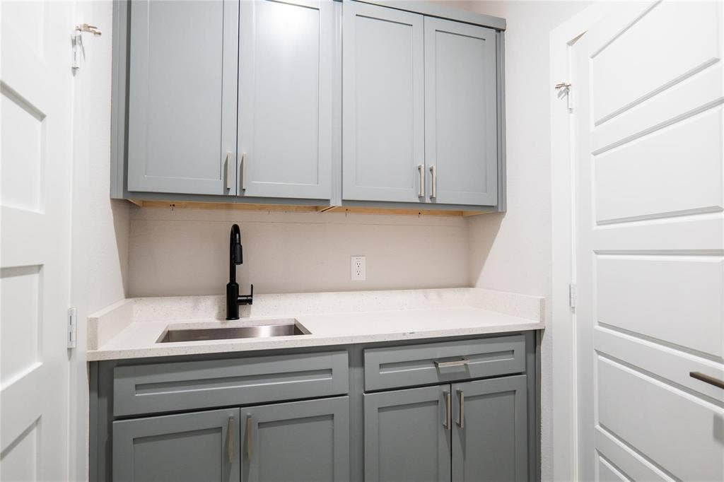 Gray cabinetry featuring brushed nickel hardware, neutral solid-surface countertop, stainless steel undermount sink, and matte black high-arch faucet